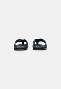 Sandale negre cu brant textil, prezentând o curea împletită și un talpă texturată cu brand alb. Design simplu, plat, cu o talpă căptușită.