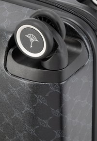 Zwarte harde koffer met een textuurafwerking en subtiel patroon. Heeft een ontwerp met een soepele wielen en een gemarkeerde accent nabij de handvat.