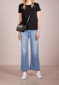 T-shirt nera a collo rotondo, jeans a gamba larga blu chiaro, sneakers bianche e una piccola borsa nera a tracolla con dettaglio di catena metallica.