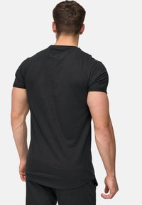 Camiseta de algodón negra de manga corta, con un escote redondo y un dobladillo trasero ligeramente más largo. Textura suave, sin patrones visibles.