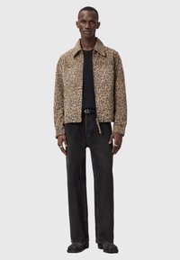 Μπουφάν με σχέδιο λεοπάρ από υφή ύφασμα· συνδυασμένο με μαύρο μπλουζάκι και σκούρο τζιν. Το μοντέλο στέκεται πρόσωπο με το κοινό με ουδέτερο φόντο.