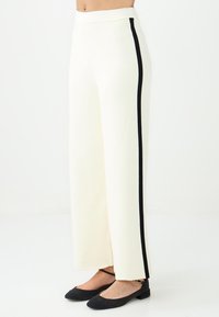 Wijdvallende broek van off-white stof, met zwarte zijstrepen. Soepele textuur met een hoge taille en subtiele plooidetails.
