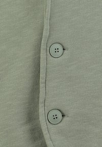 Primer plano de una tela de punto de color verde claro con dos botones redondos verdes abrochados a través de los ojales.