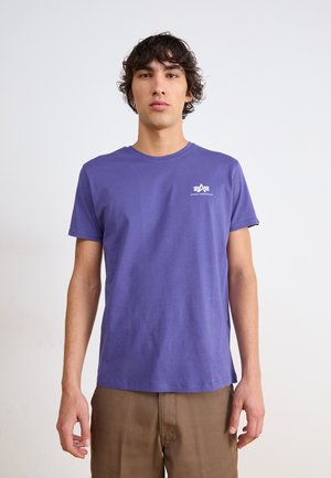 Purple cotton t-shirt with a crew neck, short sleeves, and a white "Alpha Industries" logo on the left chest. Smooth texture.