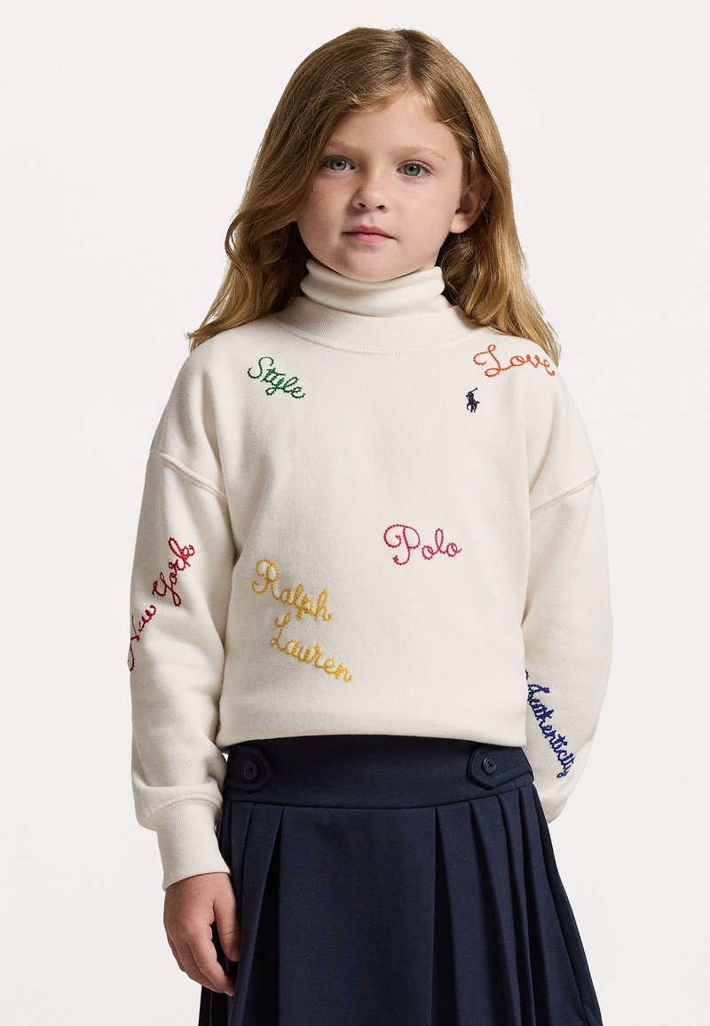 Sweatshirt de gola alta branca com texto bordado colorido, incluindo "Estilo," "Amor," e "Polo." Usado com uma saia plissada azul-marinho.