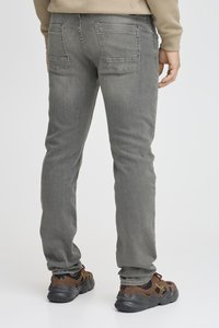 Vaqueros de denim gris claro con un diseño ajustado, cinco bolsillos y costuras de contraste en los bolsillos traseros. Llevados con zapatillas oscuras.