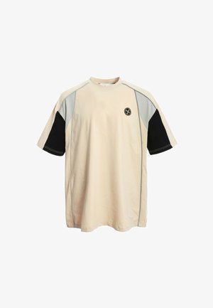 Camiseta oversized beige con mangas contrastantes en negro y gris, cuello redondo y parche de logo en la parte delantera, hecha de una suave mezcla de algodón.