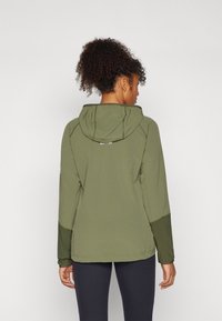 Zaļš kapucej jackets ar teksturētu audumu, ar sašutu kapuci, kontrastējošām piedurknēm un vidēju garumu.