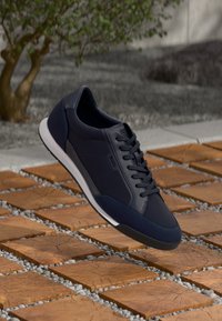 Dark blue sneakers with a smooth leather upper, textured accents, and a white rubber sole, featuring a lace-up design and branding.