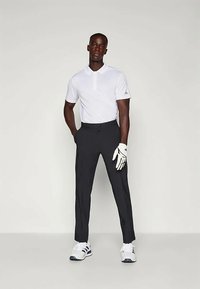 Λευκό polo μπλουζάκι, σκούρο γκρι παντελόνι, άσπρο γάντι γκολφ και αθλητικά παπούτσια. Το ντύσιμο είναι σχεδιασμένο για γκολφ, με κλασική εφαρμογή.