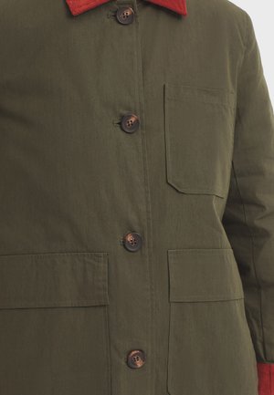 Veste verte avec un col en velours côtelé rouge, dotée de quatre poches avant et de boutons marron, fabriquée dans un tissu lisse et texturé.