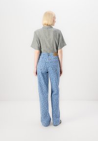 Γκρι λινό πουκάμισο με κοντά μανίκια, συνδυασμένο με ανοιχτόχρωμα μπλε τζιν με λουλουδάτο σχέδιο. Η πίσω πλευρά τονίζει την ετικέτα στη μέση.