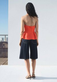 Red peplum top paired with dark blue wide-leg denim shorts, structured design with a smooth texture, black strappy sandals.