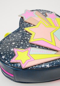 Heart-shaped bag with a navy glitter exterior, features colorful star appliqués in pink, yellow, and pastel colors. Zippered closure with pink accent.