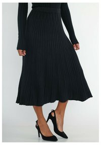 Jupe midi plissée noire en tissu côtelé, dotée d'une taille ajustée et d'un ourlet évasé, assortie à des chaussures à talons hauts noires.