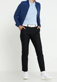 Marinblå quiltad jacka över en ljusblå pikétröja, kombinerad med svarta slim-fit byxor och vita sneakers. Inkluderar ett vitt skärp och texturerade tyger.