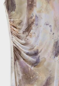 Gros plan d’un tissu tie-dye beige et violet avec des fronces réunies sur un côté créant des plis doux et une texture.