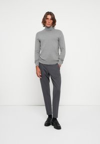 Siv turtleneck pulover iz mehke pletenine, v kombinaciji s slim-fit temno sivimi hlačami. Črni mokasini dopolnjujejo videz. Minimalistična zasnova na beli podlagi.