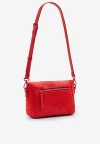 Czerwona skórzana torba na ramię z tłoczonym wzorem kwiatowym, zapinaną na zamek kieszenią z przodu i regulowanym paskiem. Teksturowana powierzchnia i prostokątny kształt.