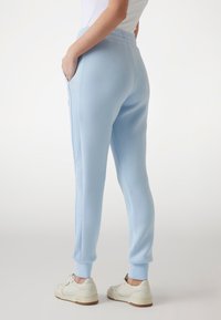 Light blue joggers made of soft fabric, featuring side pockets, elastic waistband, and ribbed cuffs. Worn with white sneakers.