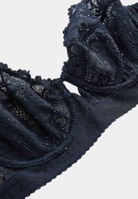 Marineblaue Spitzen-Bralette mit Rüschenspitze und subtil schimmernden Details. Verfügt über einen strukturierten Bund für zusätzlichen Halt und filigrane Blumenmuster.