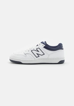 Weißer und marineblauer Sneaker in niedriger Ausführung mit perforierter Spitze, Schnürung vorne und großem "N" Logo an der Seite.