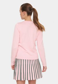 Haut rose clair à manches longues avec un col rond, associé à une jupe plissée avec des rayures verticales vertes. Texture de tissu lisse.