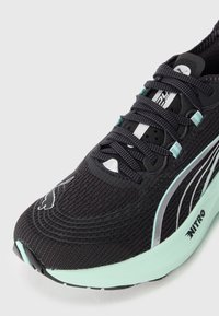 Gros plan sur une chaussure de course noire avec une semelle vert menthe, des lacets noirs, le logo Puma sur le bout et le marquage "Nitro" sur le côté de la semelle.