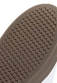 Semelle de chaussure en caoutchouc marron avec un motif texturé de bosses circulaires espacées régulièrement et un bord à motif pour une meilleure adhérence.