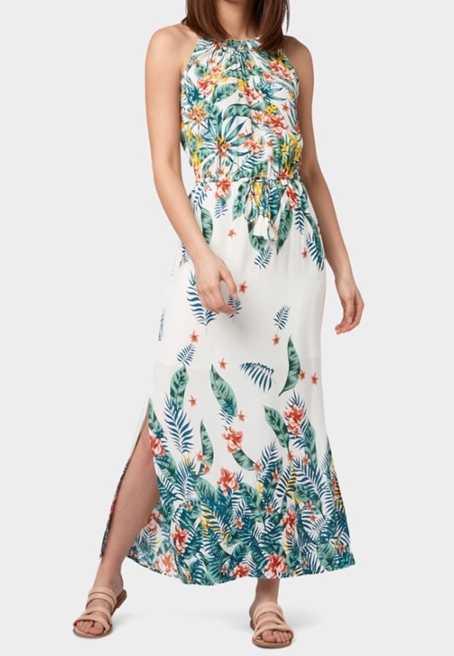 Robe maxi blanche sans manches avec imprimé de feuilles tropicales vertes et orange ainsi que des fleurs, fendue sur le côté, ceinture tressée à la taille, portée avec des sandales beige.