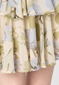 Rochie florală cu un fundal crem, decorată cu modele botanice în nuanțe de albastru deschis și verde, cu volane suprapuse și un material fluid, ușor.