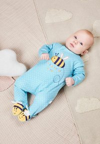 Hellblauer Einteiler mit weißen Punkten, der ein Bienenmotiv und bunte Schriftzüge zeigt. Enthält weiche gelbe Bienenhausschuhe mit gestreiften Akzenten.