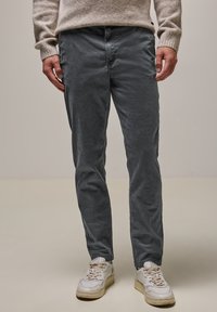 Šedé kordové kalhoty s texturovaným vzorem, slim fit, se bočními kapsami, spárované s bílými teniskami.