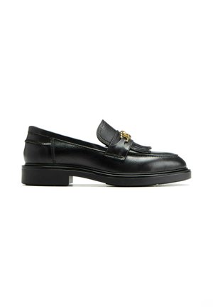 Mocassins en cuir noir avec une semelle plate, présentant une frange décorative et des accessoires en ton doré sur la sangle. Texture lisse et design classique.