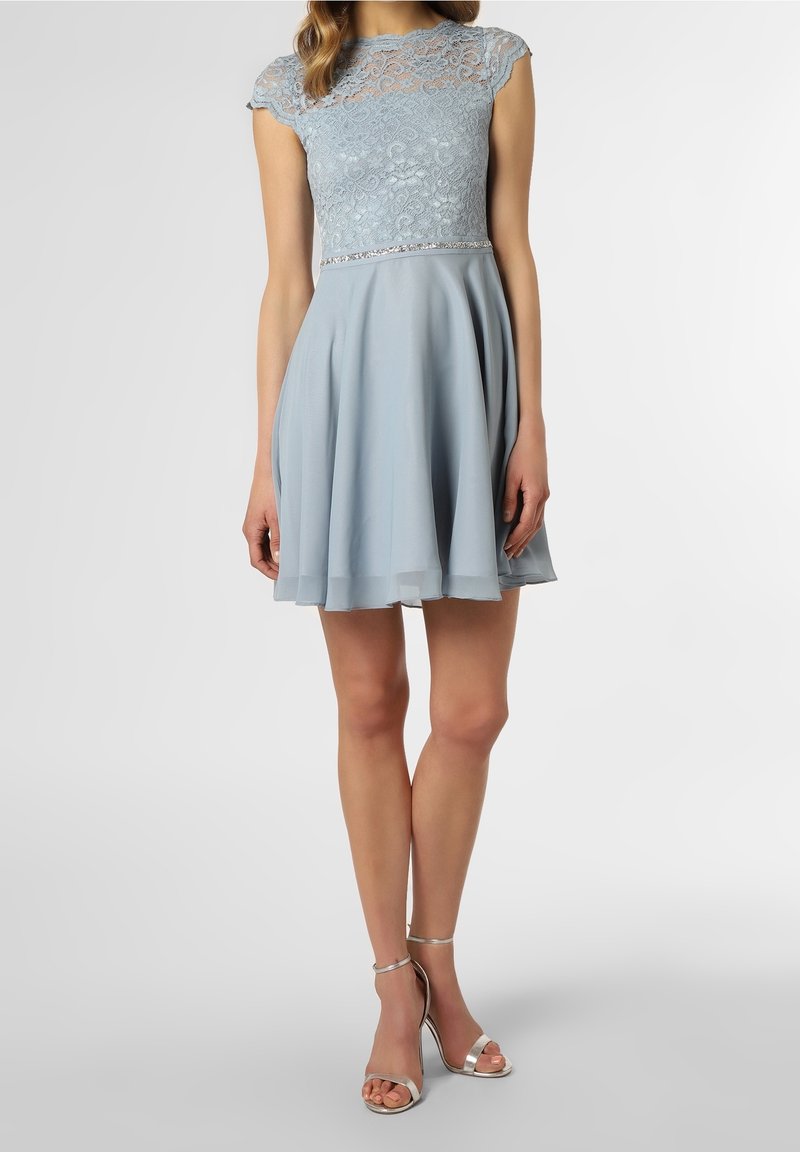 Robe bleu clair avec un corsage en dentelle, des manches courtes et un détail argenté à la taille. Jupe évasée et tissu léger. Associée à des talons argentés.