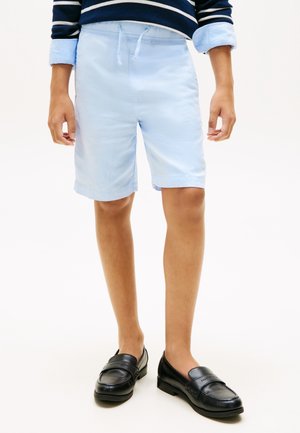 Băiat purtând pantaloni scurți albaștri deschis cu șnur, pantofi loafers negri și o cămașă cu mâneci lungi, navy cu dungi, cu manșete rostogolite.