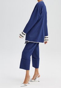 Tmavě modrý sako oblek s dlouhým sakem s bílým lemováním a kalhotami s volným střihem do délky nad kotníky. Rukávy s bílými a černými pruhy. Kovové lodičky na vysokém podpatku.