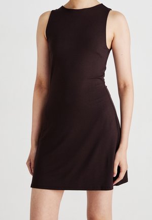 Mouwloze zwarte jurk met een hoge hals, getailleerde taille en boven de knie-lengte, gedragen door een staand persoon tegen een effen witte achtergrond.