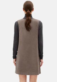 Graues Baumwollcordkleid mit geradem Schnitt, ärmellos, über dem Knie geschnitten, getragen über einem dunkel gestreiften langärmligen Hemd. Einfache und strukturierte Oberfläche.