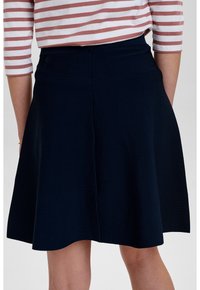 Laivastonsininen kellotettu hame, joka on valmistettu teksturoituneesta kankaasta, ja siinä on sulava vyötäröosa sekä takasauma. Yhdistetty raidoitettuun paitaan kontrastiksi.