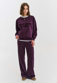 Fialová mikina s textem "bylo nebylo", doplněná o odpovídající fialové kalhoty. Volný střih, měkká látka a leopardí slip-on boty.