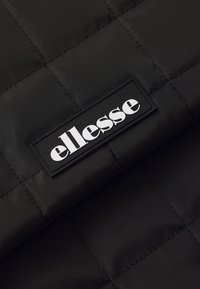 Sort quiltet stof med en glat tekstur, der har et rektangulært sort mærke og hvidt "ellesse" logo.