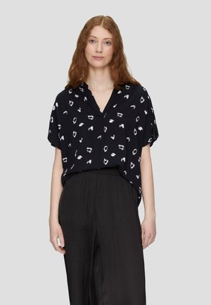 Schwarze Bluse mit kurzen Ärmeln und weißem abstraktem Muster, V-Ausschnitt, lässige Passform, kombiniert mit schwarzen, weit geschnittenen Hosen, glatte Textur.