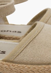 Sandalias de esparto beige con parte superior de tela trenzada y suela de cuerda de yute. Presenta finas correas a juego y un sutil detalle de costura.