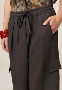 Pantalones de color gris carbón con cintura elástica y cordón, que cuentan con bolsillos laterales y un bolsillo con solapa en la pierna. Textura suave.