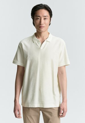 Polo de manga corta en color crema claro, hecho de tejido texturizado, con un cuello clásico y un ajuste relajado.