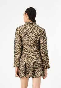 Jakna s leopardjim vzorcem, ovratnikom, dolgimi rokavi in nabranim spodnjim robom. Izdelana iz gladkega materiala, v rjavo in tan barvni shemi.