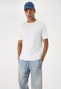 Λευκό βαμβακερό T-shirt με κοντά μανίκια, συνδυασμένο με ανοιχτό μπλε τζιν που έχουν ξεθωριασμένο εφέ και κόκκινη λογότυπο ένδειξη στην πίσω τσέπη.