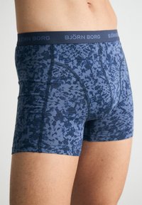 Közepes hosszúságú boxer alsónemű, kék absztrakt mintával, rugalmas pamutból készült, elasztikus derékkal, amelyen a "BJÖRN BORG" felirat látható.