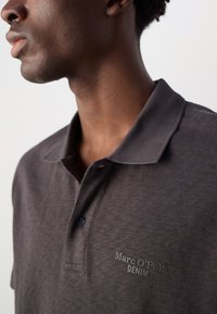 Mørkegrå polo skjorte med klassisk krave, med en subtil logo "Marc O'Polo DENIM" i matchende broderi. Myk, teksturert stoff.